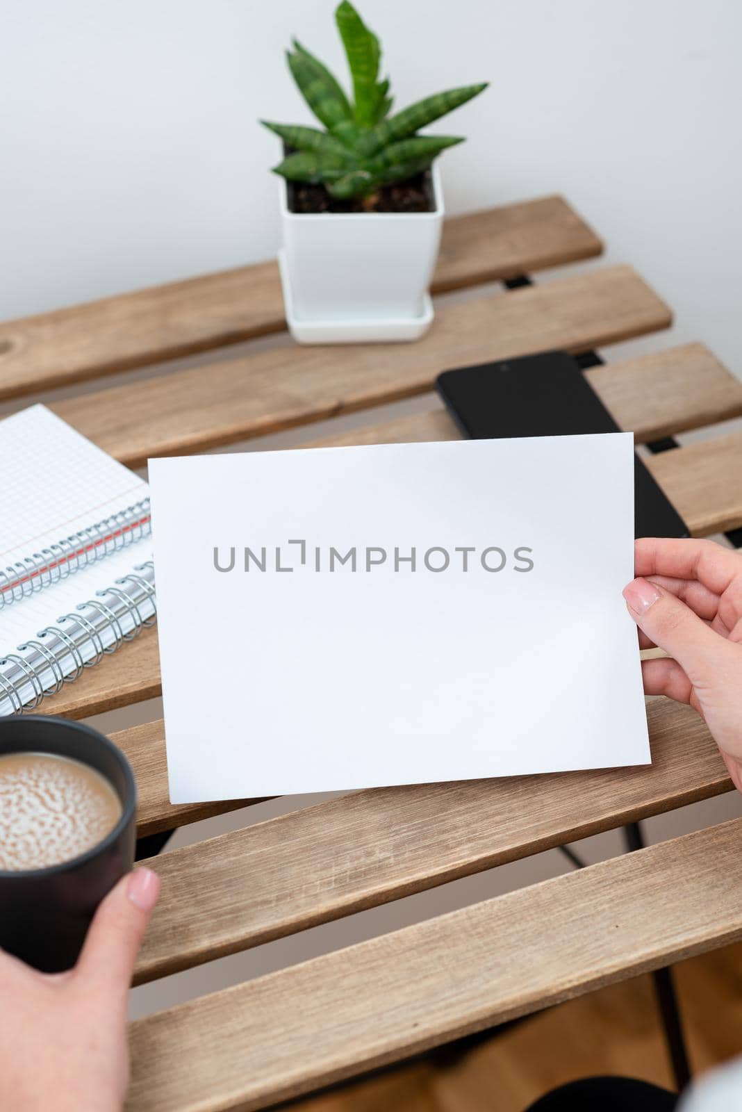 Woman Holding Important Message On Paper On Table With Coffee, Notebooks, Phone And Plant. Businesswoman Presenting Crutial Information On Note. Lady Showing New Ideas On Memo by nialowwa