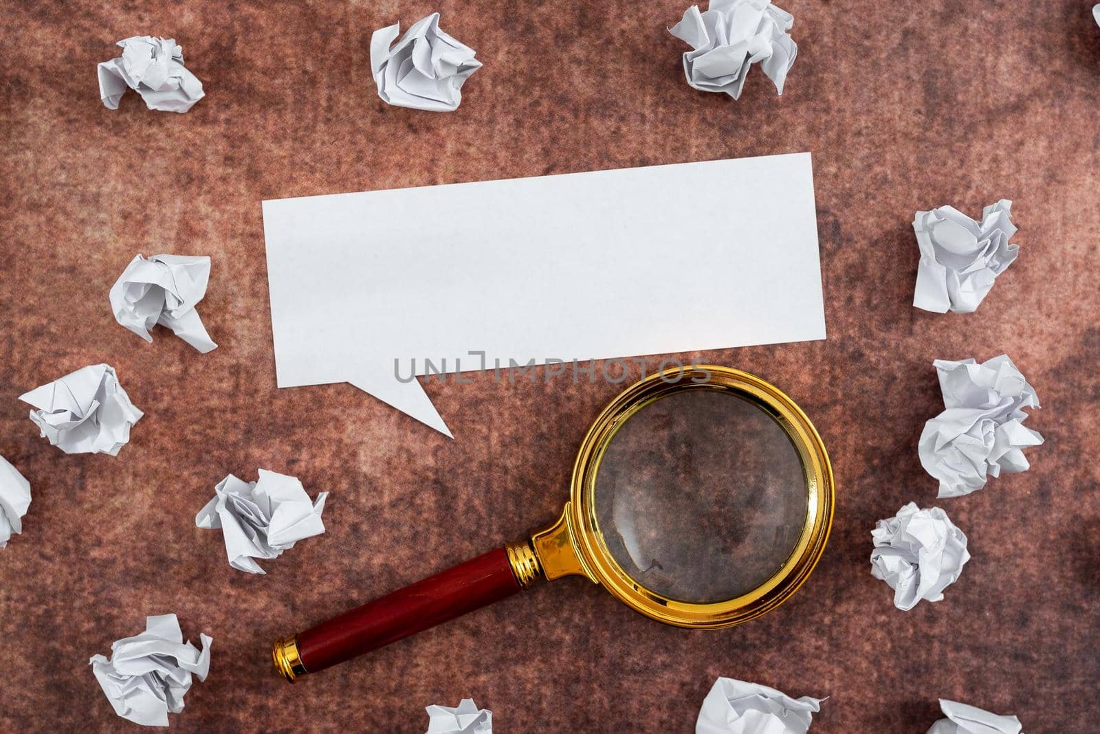 Speech Bubble Made Of Sheet With Magnifying Glass Surrounded With Crumpled Papers Over Wooden Background. It Is Showing Different Thoughts And Analyzing Strategies. by nialowwa