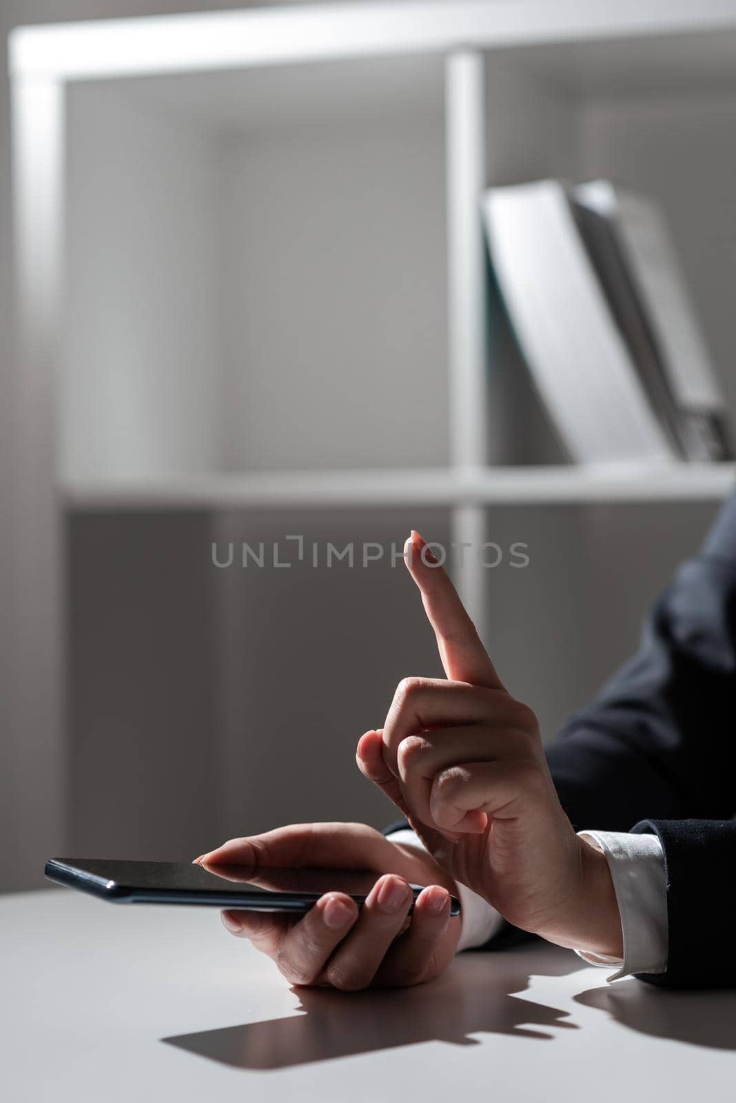 Businesswoman Holding Tablet In One Hand And Pointing With One Finger On Important Message. Sitting Woman In Office With Cellphone In Hand Presenting Informations. by nialowwa