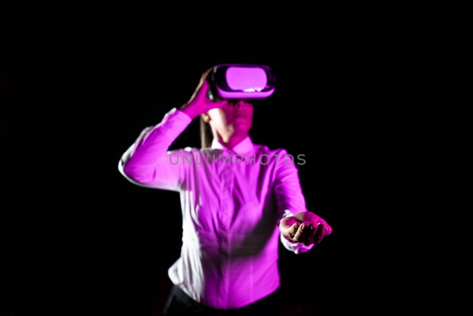 Female Manager Wearing Virtual Reality Goggles Gesturing While Taking Professional Training. Light Falling On Woman Using Gadget And Presenting Futuristic Technology. by nialowwa