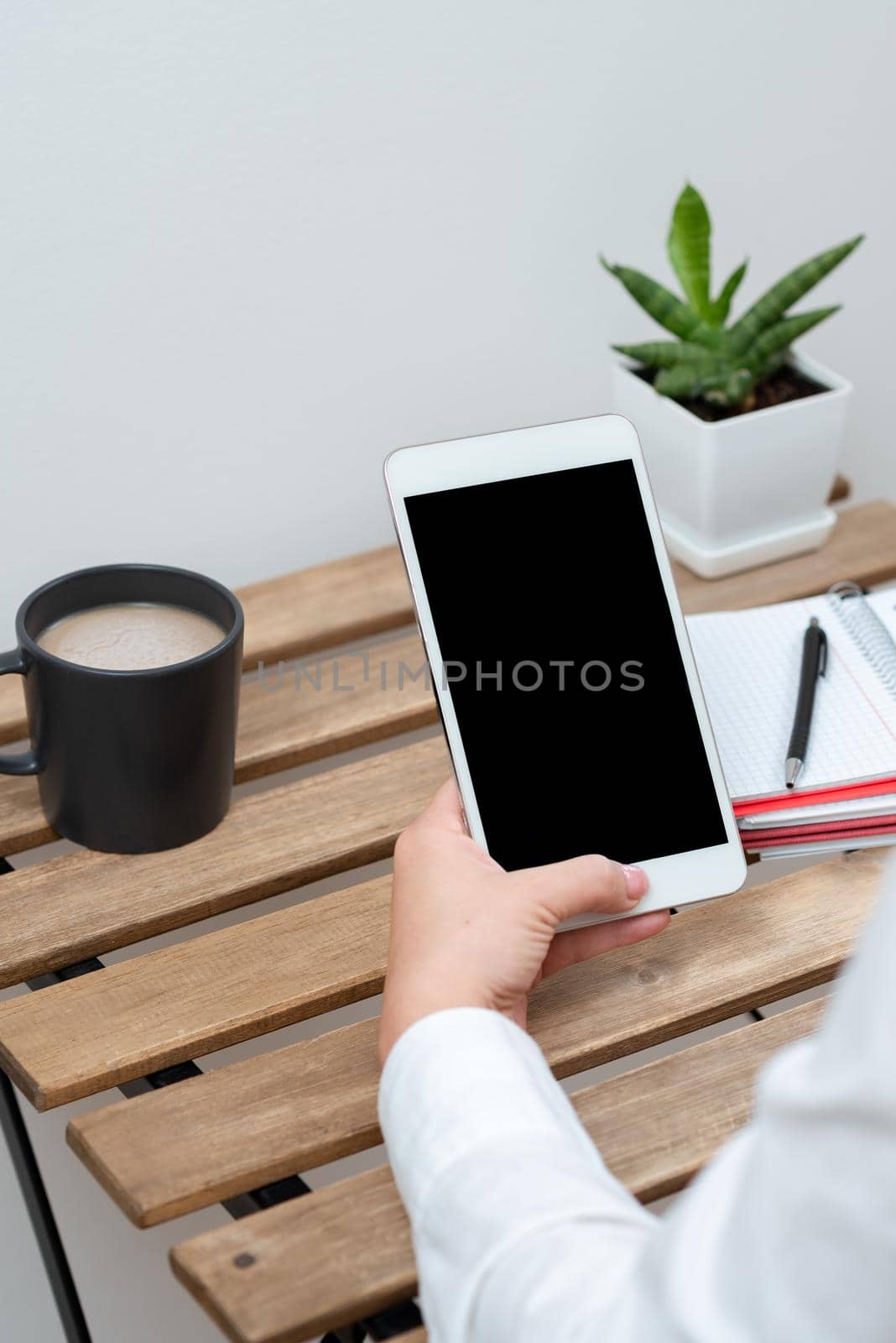 Woman Holding Tablet With Important Message On Table With Coffee, Pen, Notebooks And Plant. Businesswoman Presenting Crutial Information On Cellphone. by nialowwa