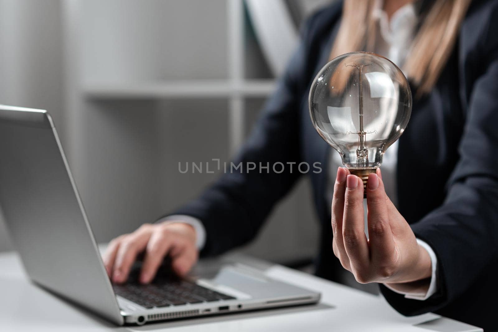 Businesswoman Typing Recent Updates On Lap Top On Desk Holding Lightbulb.