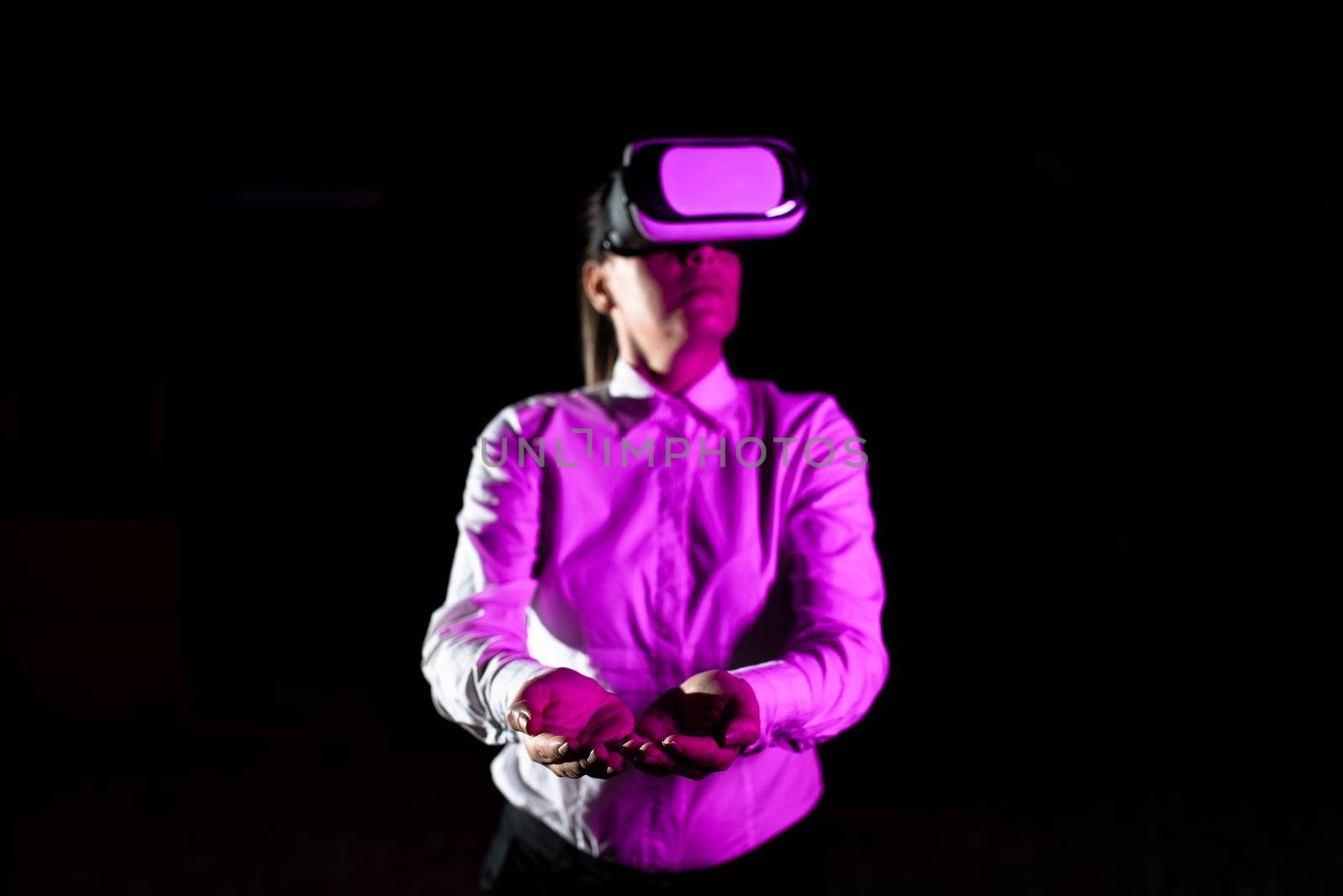 Female Manager Wearing Virtual Reality Goggles Gesturing While Taking Professional Training. Light Falling On Woman Using Gadget And Presenting Futuristic Technology. by nialowwa