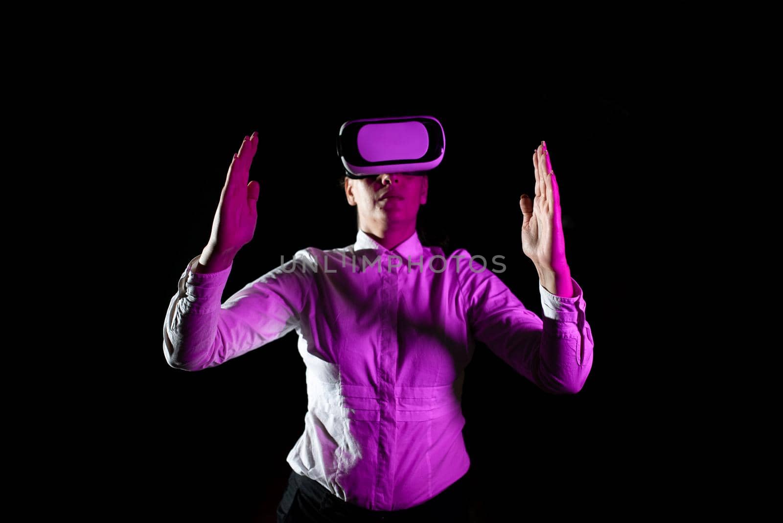 Businesswoman Using Virtual Reality Goggles Gesturing While Taking Professional Training. Light Falling On Woman Wearing Modern Simulator And Presenting Creative Technology by nialowwa