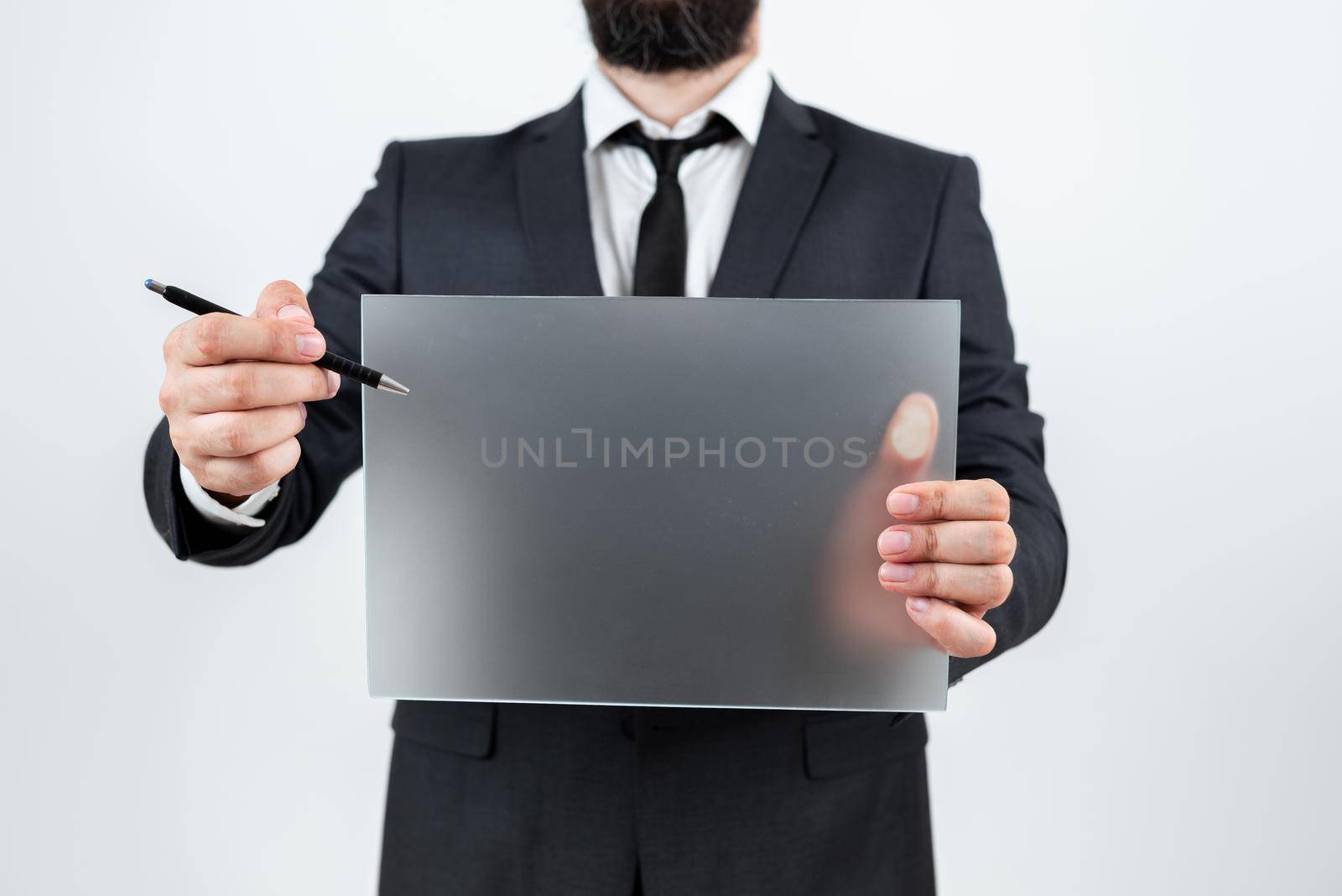 Male Professional Holding Blank Placard And Pen And Displaying Business Data. Businessman Wearing Suit Showing Rectangular Board For Marketing And Branding Of Company. by nialowwa