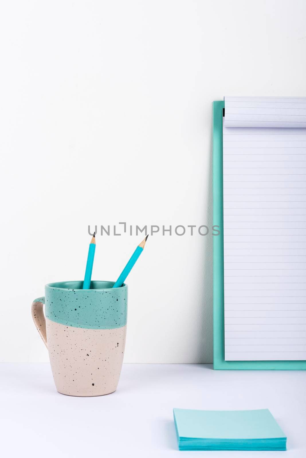 Cup With Two Pencils Inside Placed On Office Desk With Clipboard And Notes.