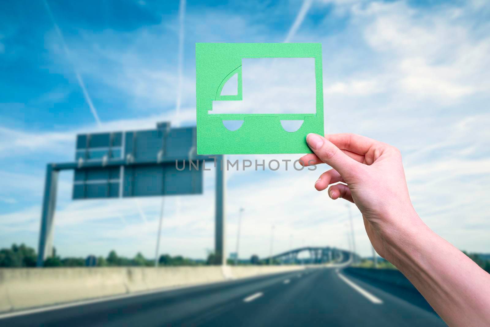 Hand holds green logistics truck symbol against highway