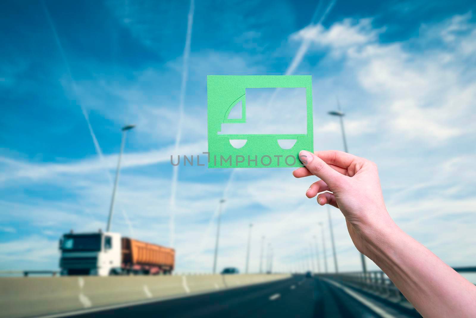 Hand holds green logistics truck symbol against highway