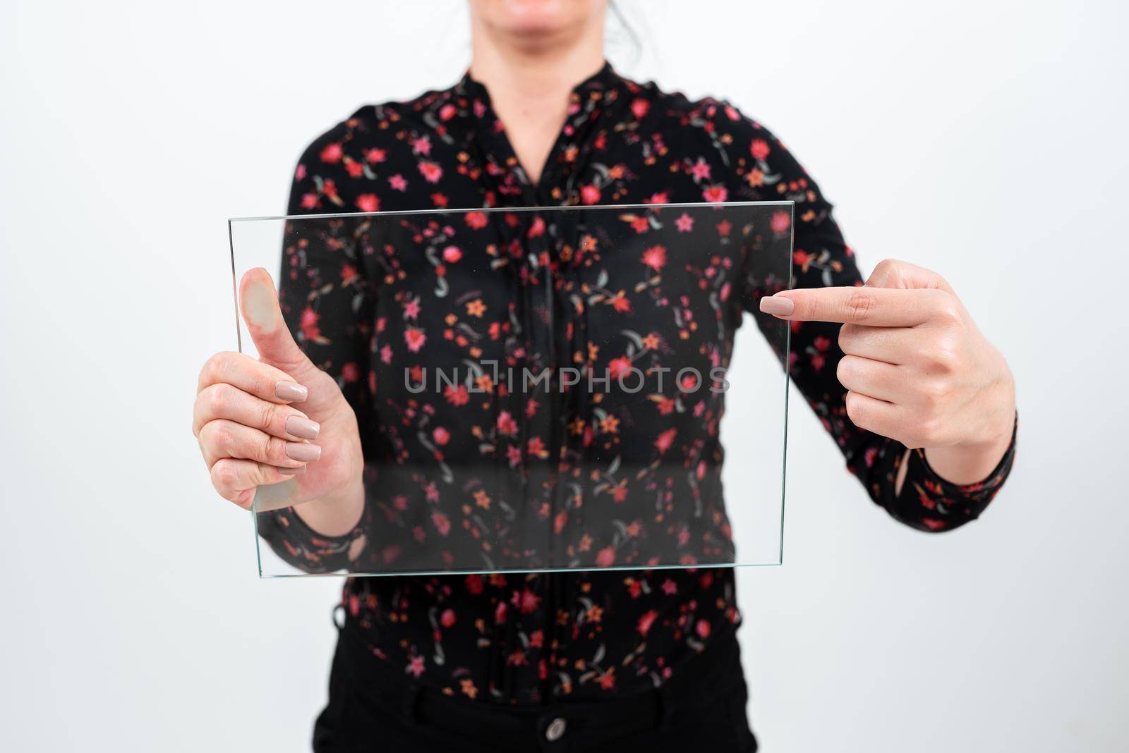 Businesswoman Holding And Pointing Transparent Glass While Presenting Important Information. Woman Wearing Floral T-Shirt Showing Rectangular Banner For Brand Promotion. by nialowwa