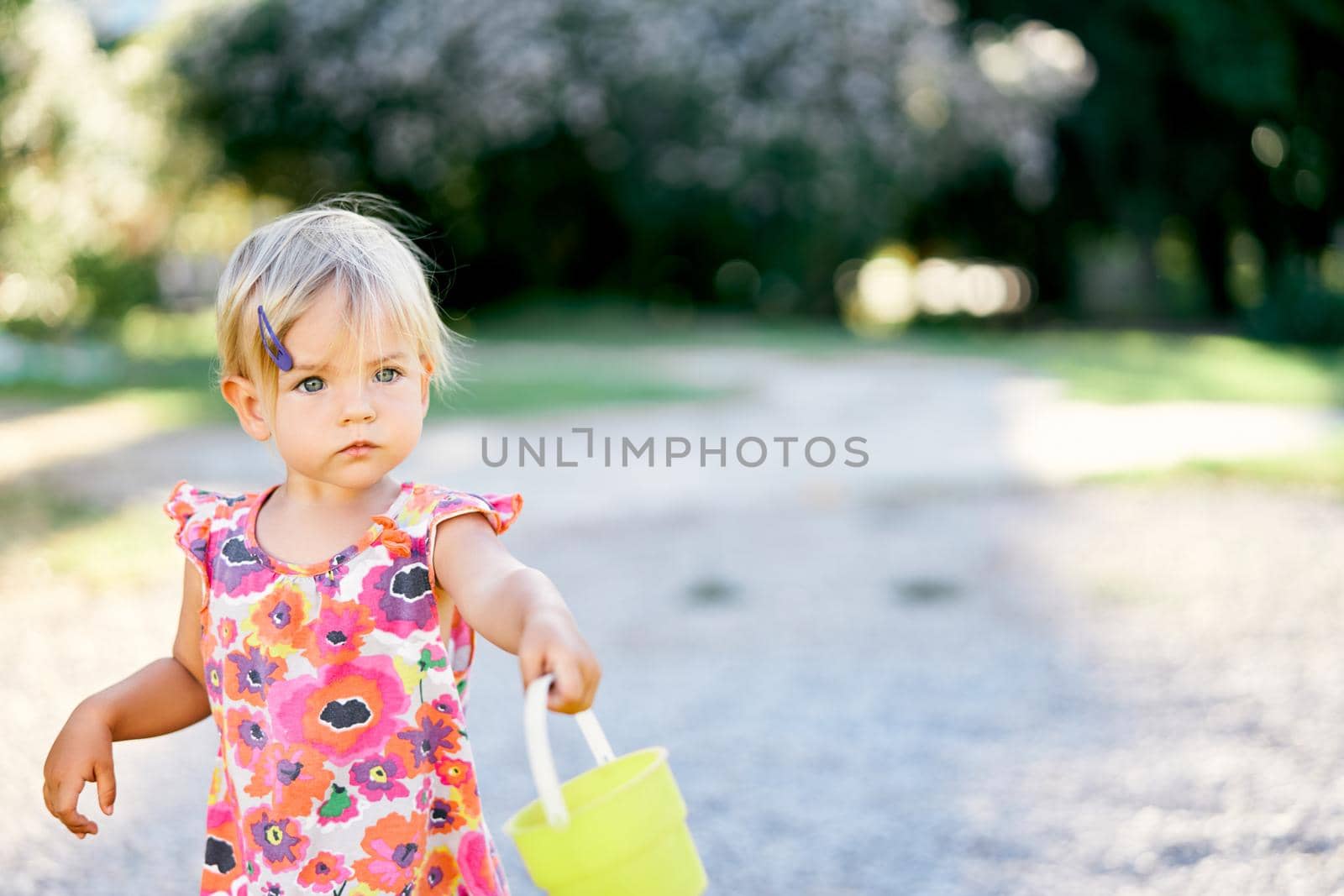 Little girl with a plastic bucket stands on the playground. High quality photo