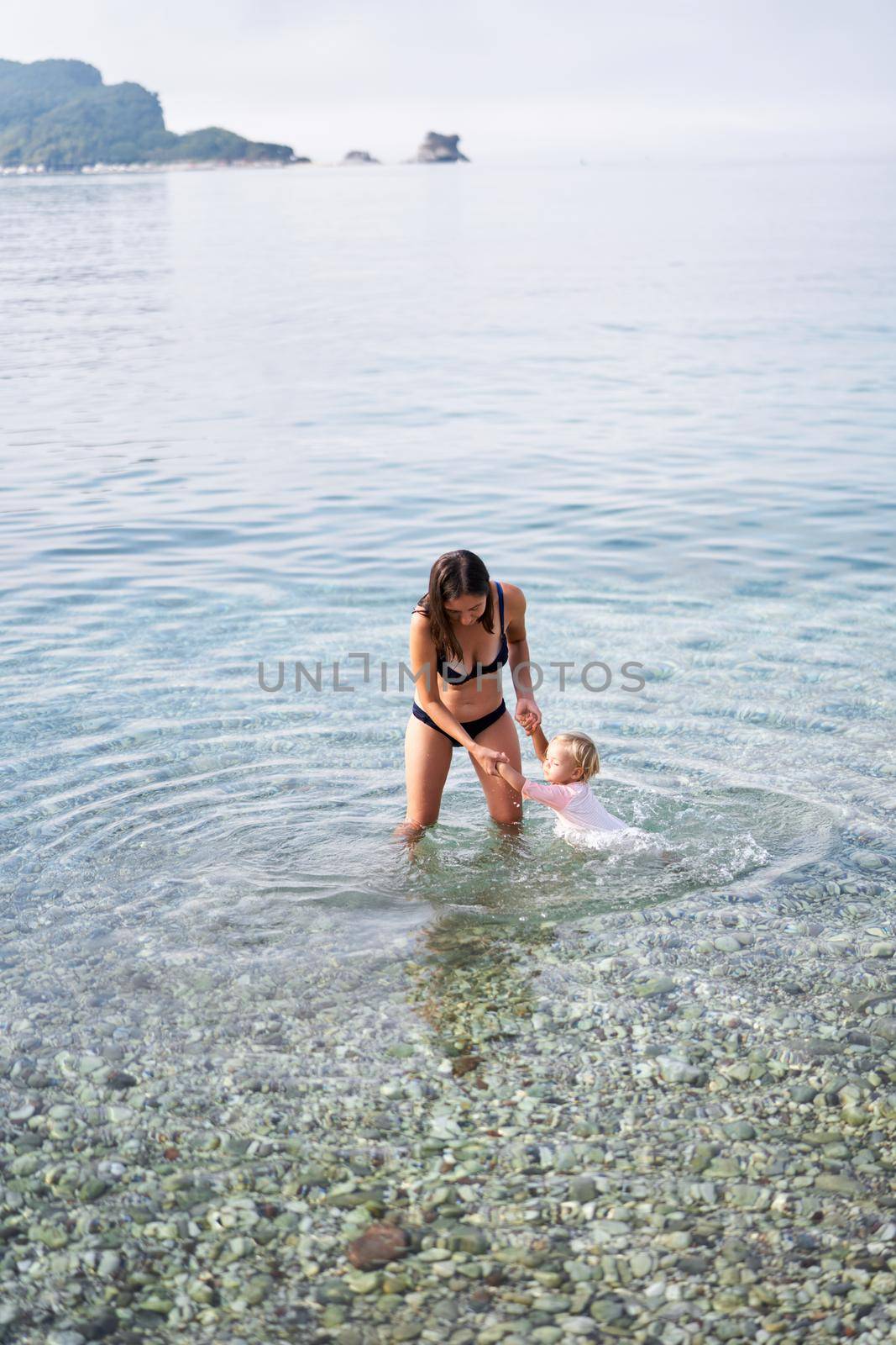 Mom teaches little girl to swim holding her hands by Nadtochiy