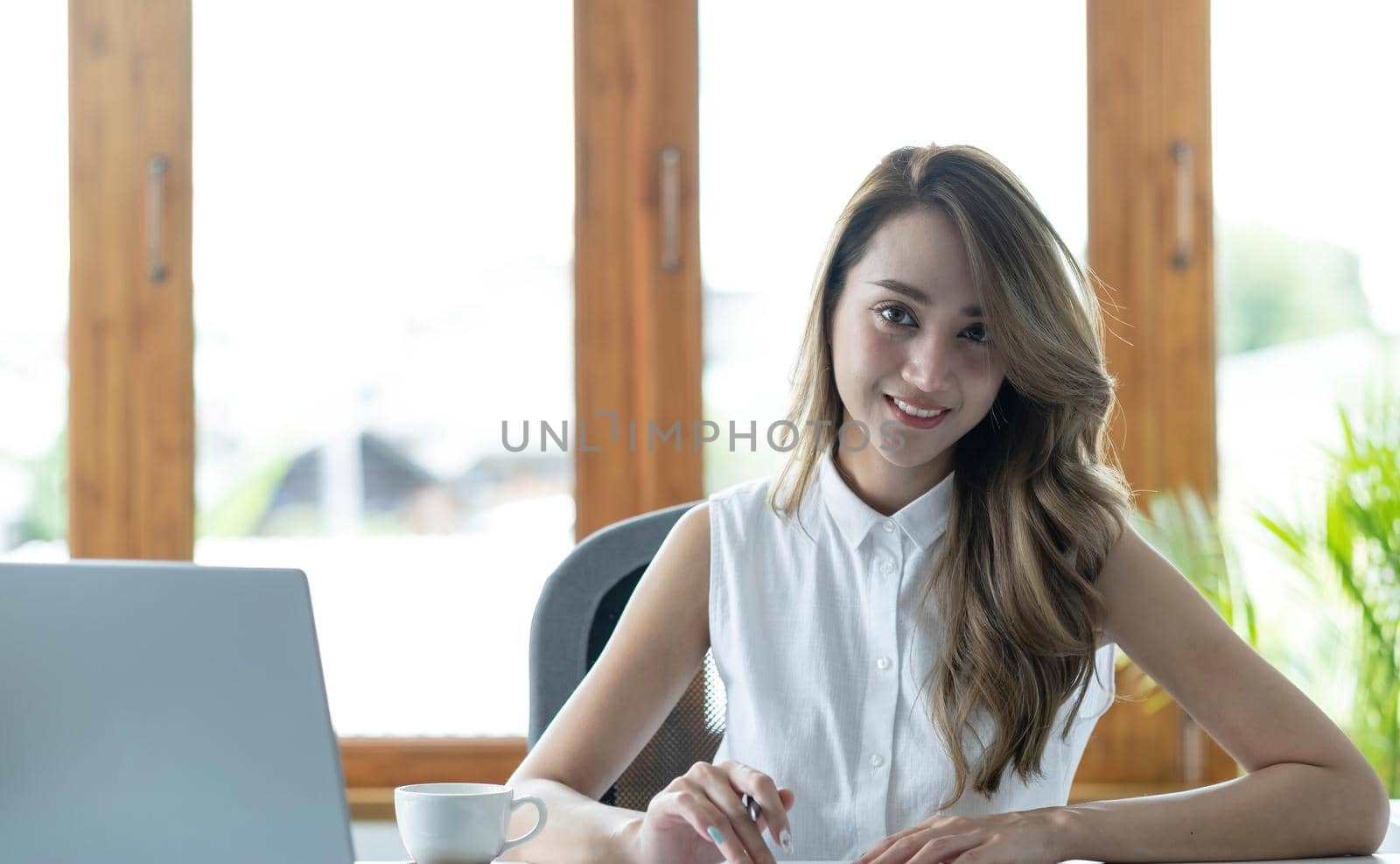 Young beautiful woman using her laptop while sitting in a chair at her working place. by wichayada
