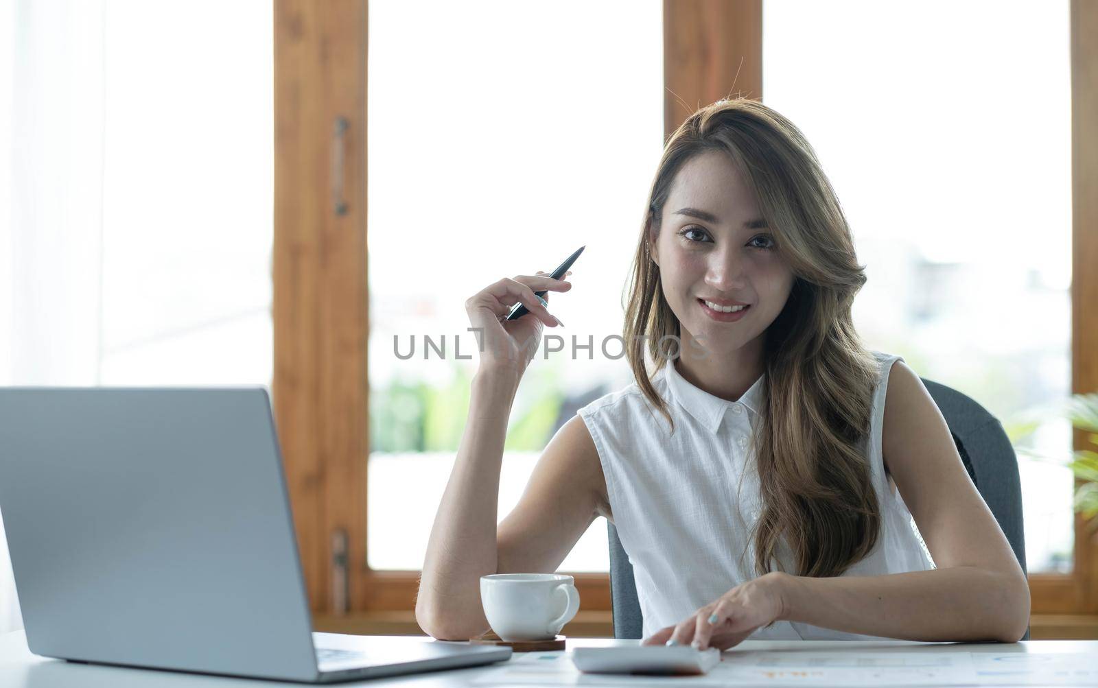 Charming Asian businesswoman working with a laptop at the office. Looking at camera..