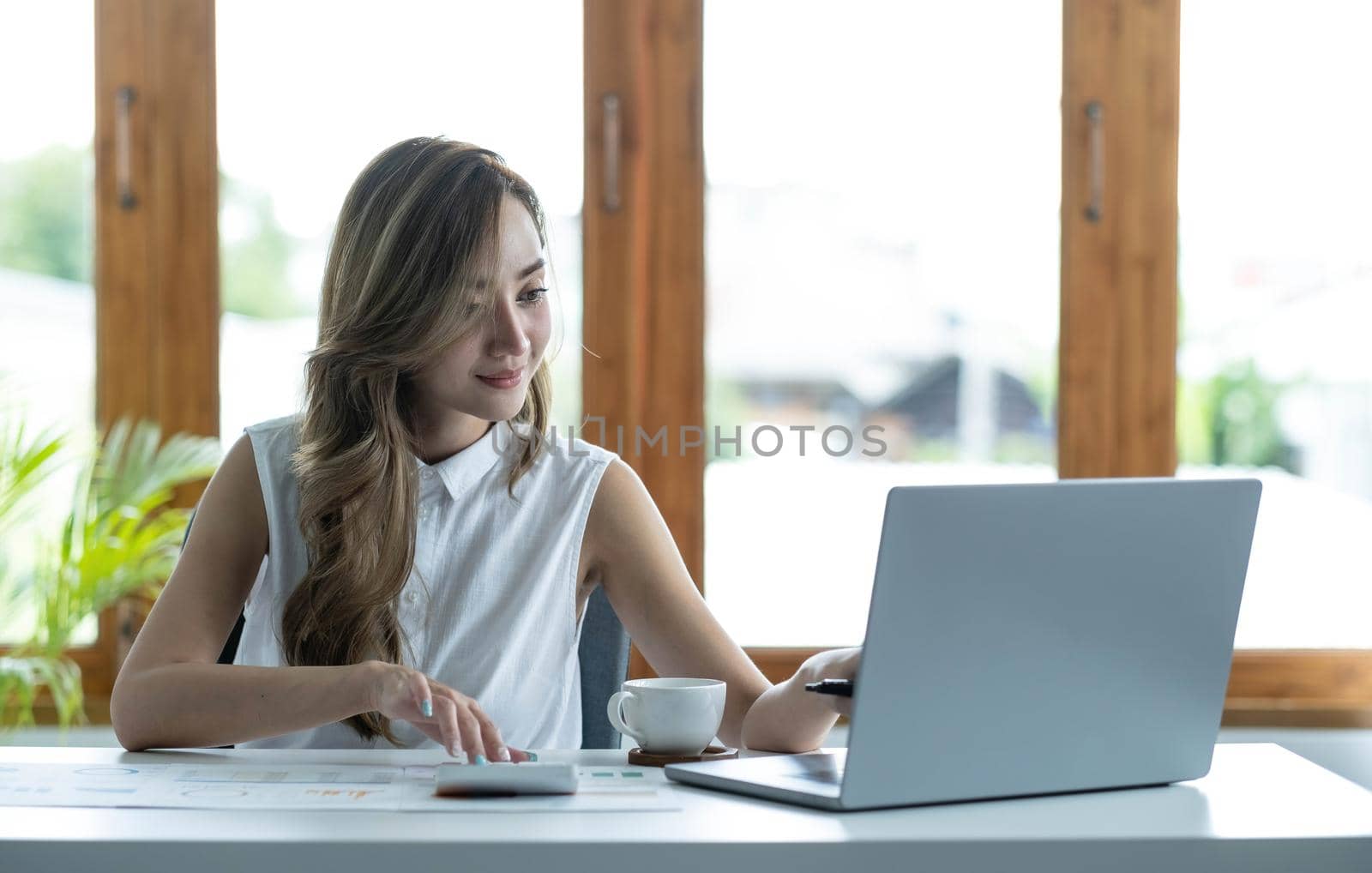 Beautiful Asian businesswoman analyzes charts using laptop calculator at the office..