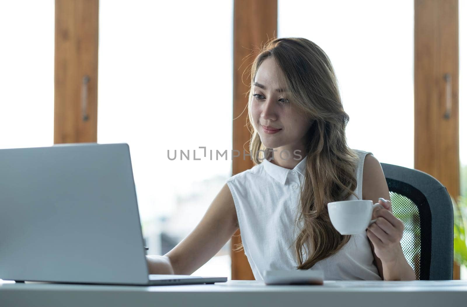 Beautiful young Asian businesswoman drinking a coffee working on laptop at office..