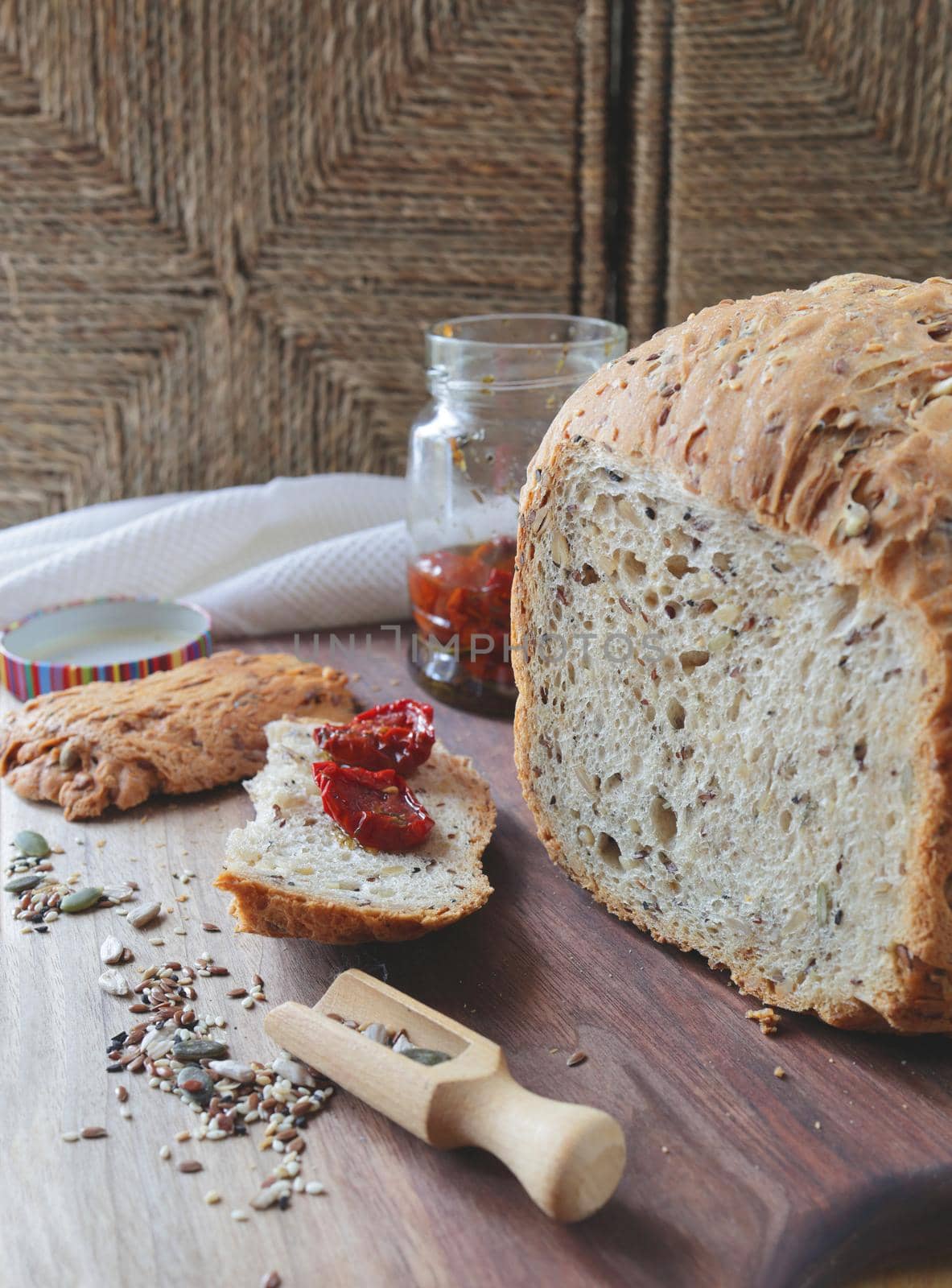loaf of homemade whole grain bread and a cut slice of bread on a wooden cutting board. A mixture of seeds and whole grains. Sun-dried tomatoes on a crust of fresh bread. Healthy food concept by Proxima13