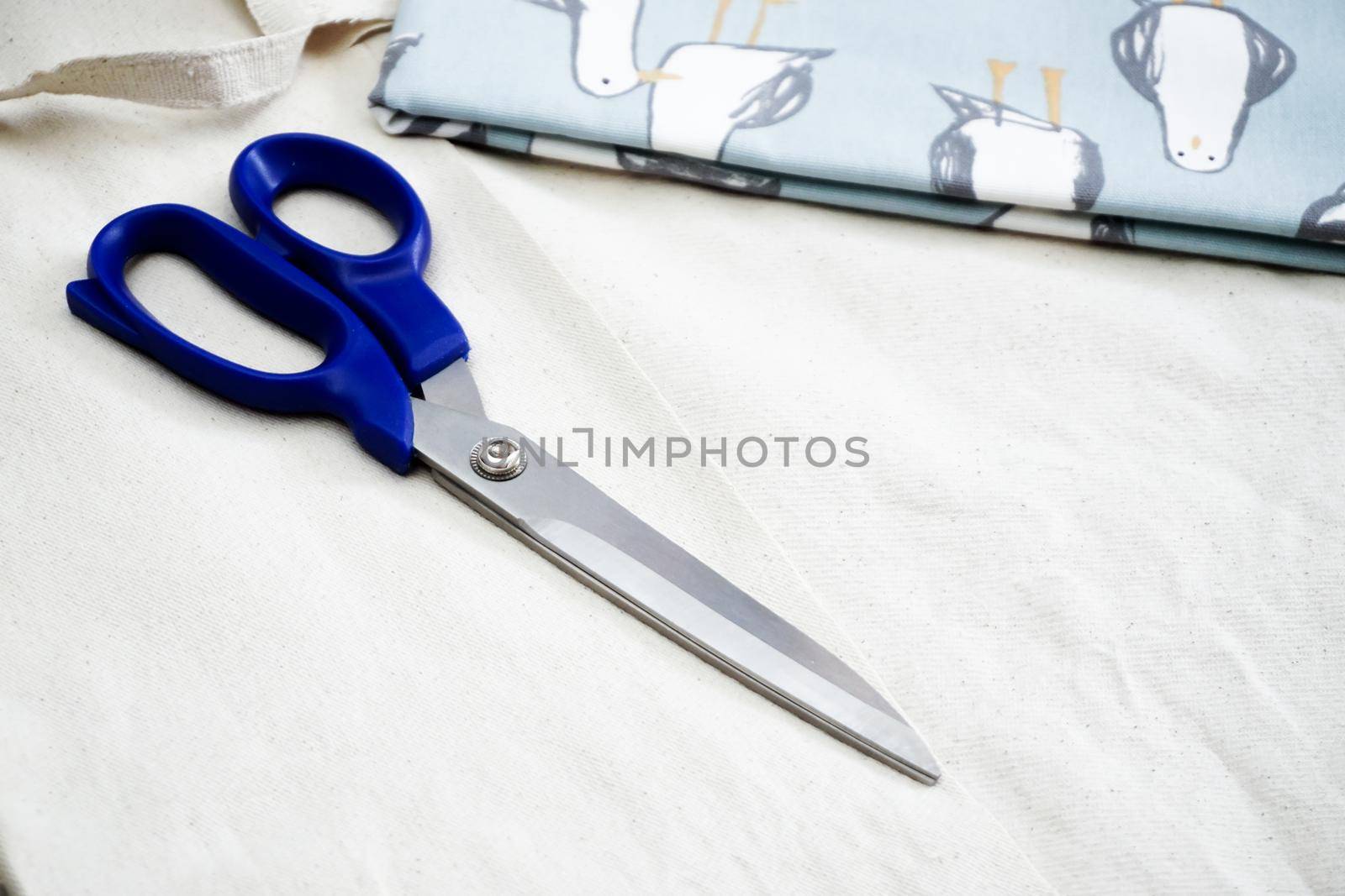 White fabric and blue scissor on isolated background close up view