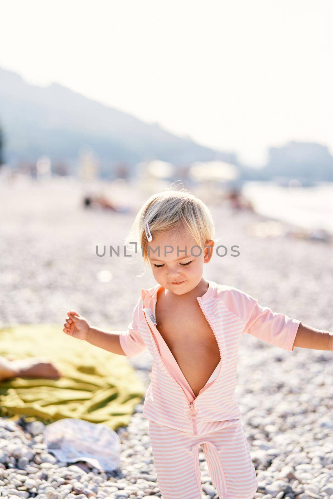 Little girl in an unzipped jumpsuit stands on the beach. High quality photo