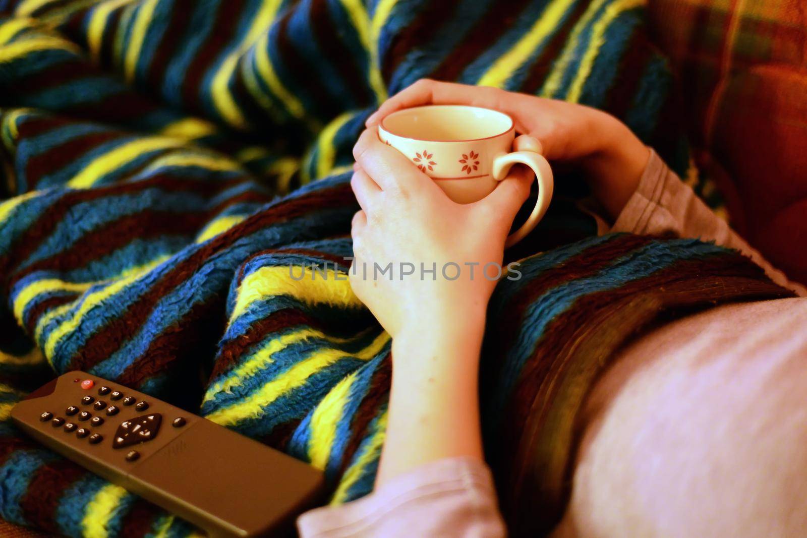 Chilling at home under the blanket with remote control and tea mug in hand
