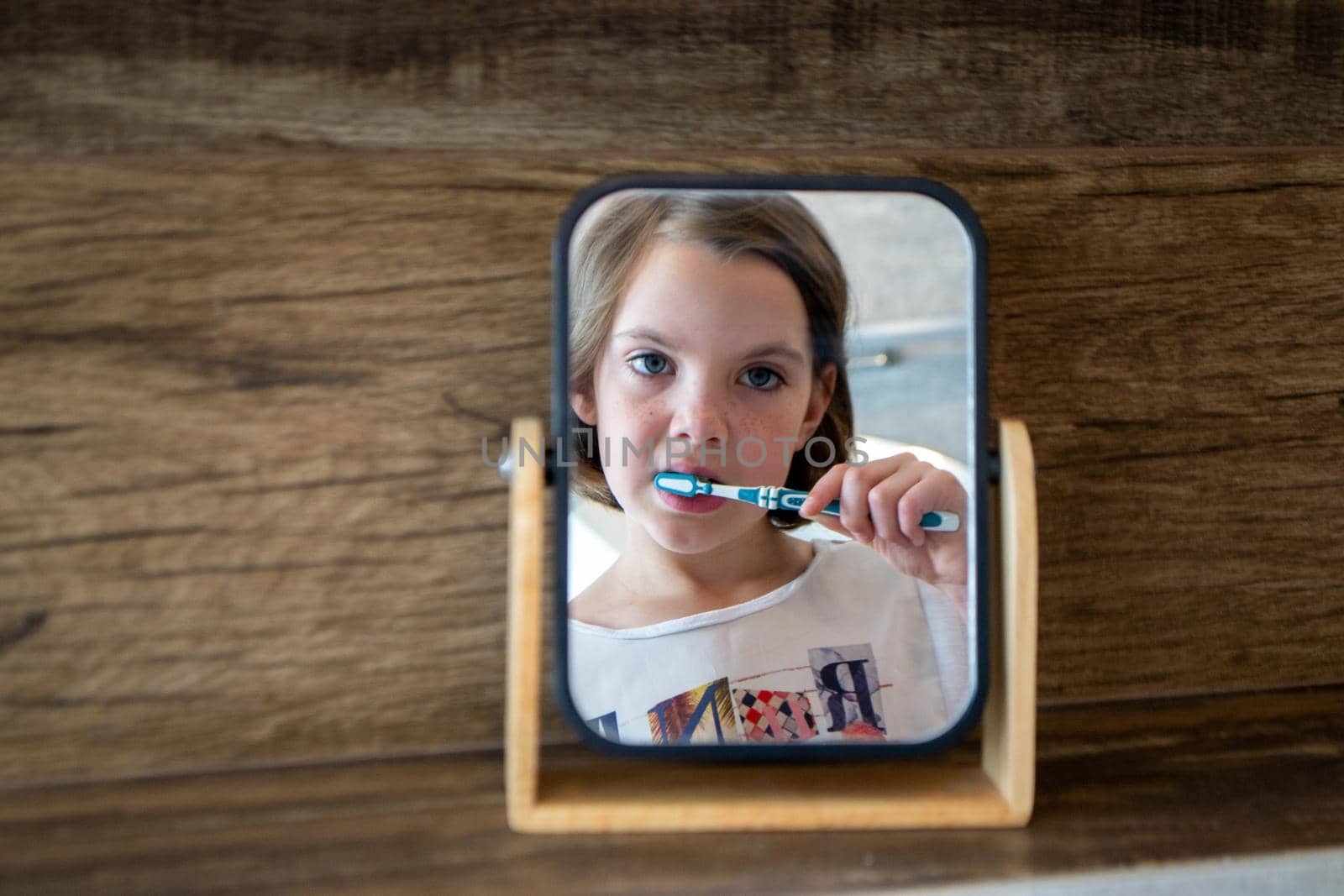 Oral hygiene, healthy teeth and care. Girl brushing teeth with toothbrush and looking in mirror in bathroom interior in the morning, closeup, empty space. High quality photo