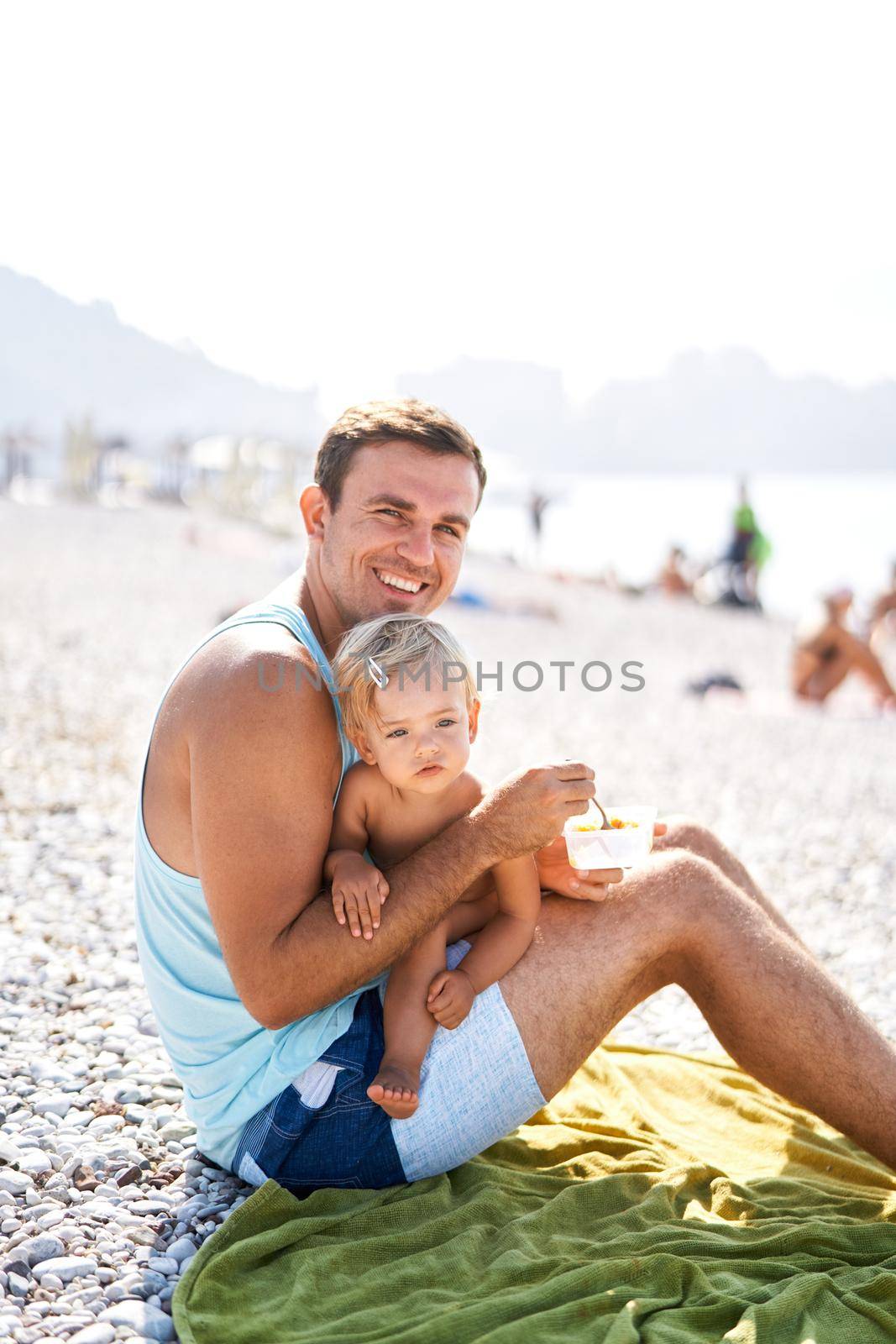 Smiling dad feeding his little daughter on the beach. High quality photo