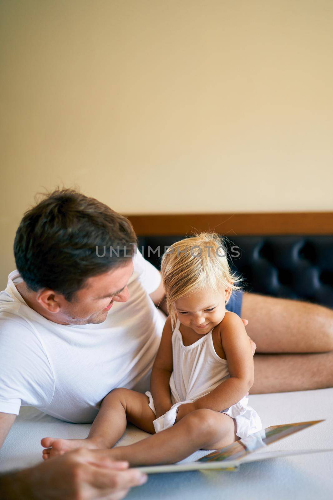 Laughing dad and little girl reading a book by Nadtochiy