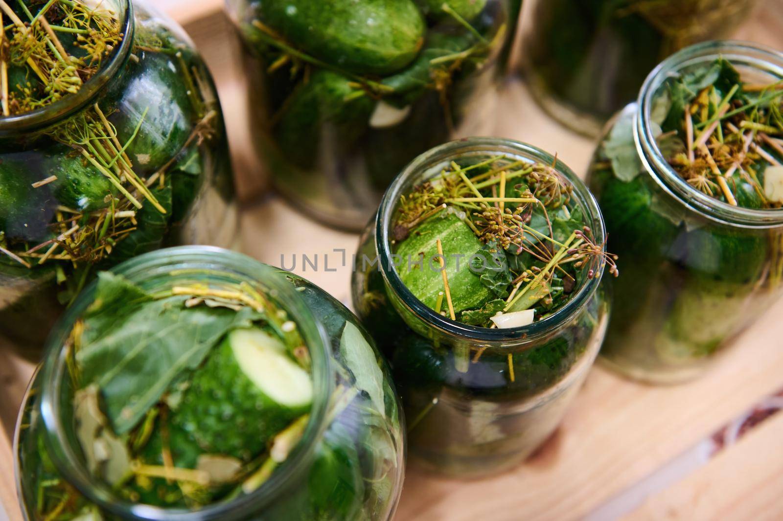 Fresh seasonal harvest of green cucumbers salted and pickled with garlic and dill, preserved in glass jars for winter by artgf