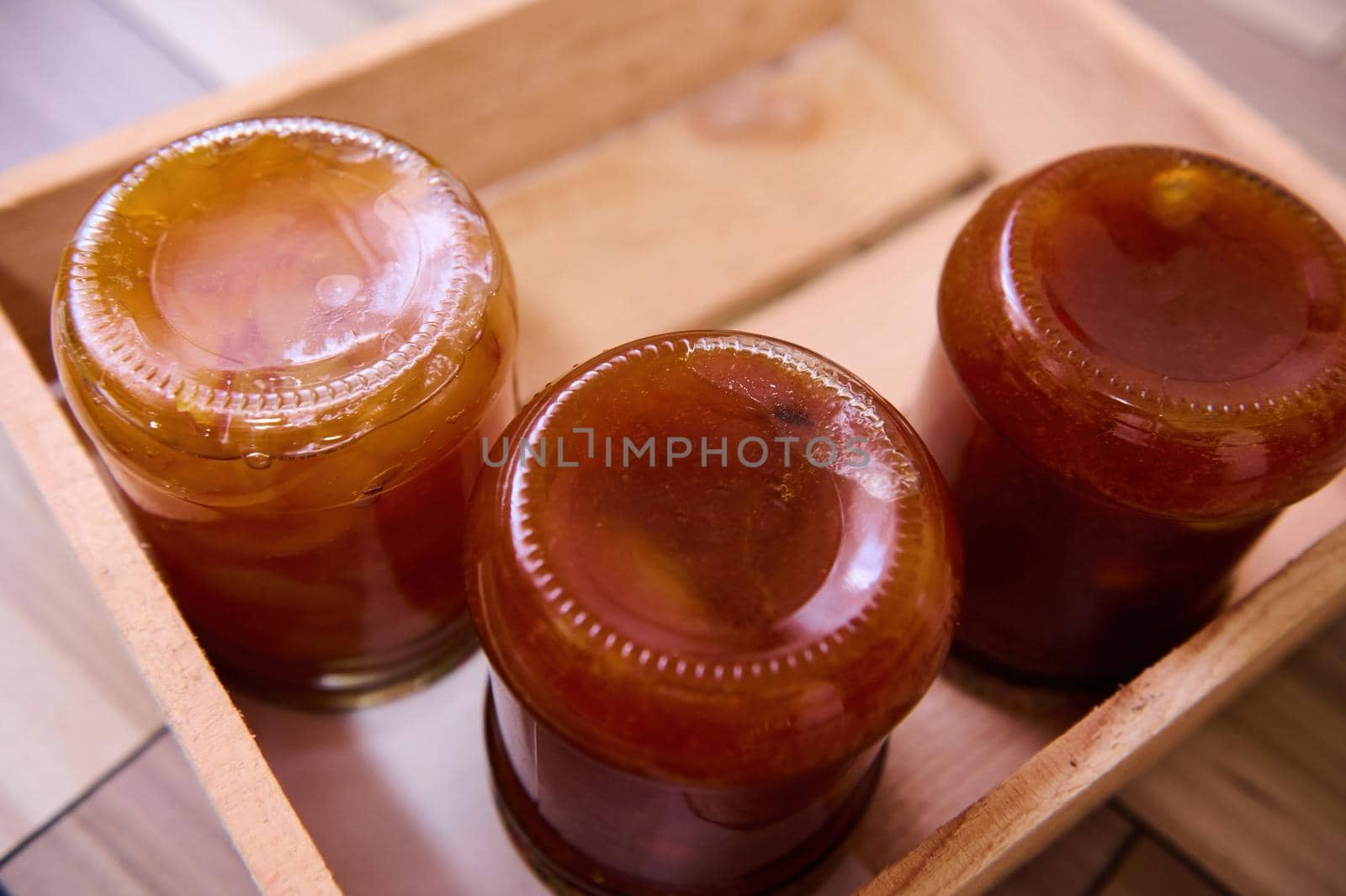 Top view of homemade apricot jam with pits and canned peach slices in glass jars upside down on wooden crate. Copy space by artgf
