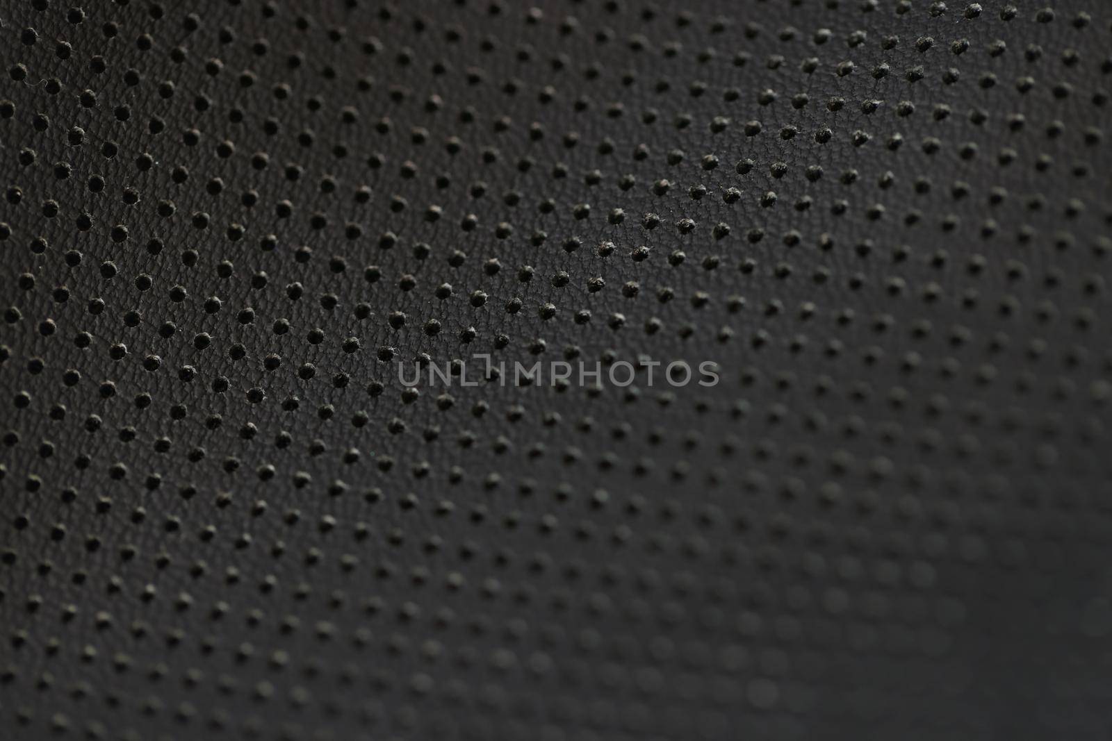 Black leather fabric pattern of small holes, close-up. Perforated matte texture. A macro shot of dark background