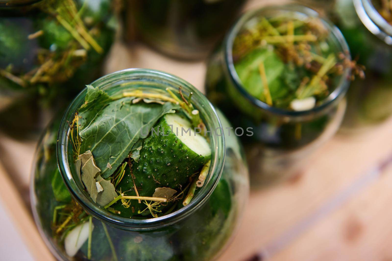 Autumn pickling and canning of vegetables. Close-up of glass jars with homemade canned cucumbers on a wooden surface. Healthy organic fermented food concept. High angle view. Family traditional recipe