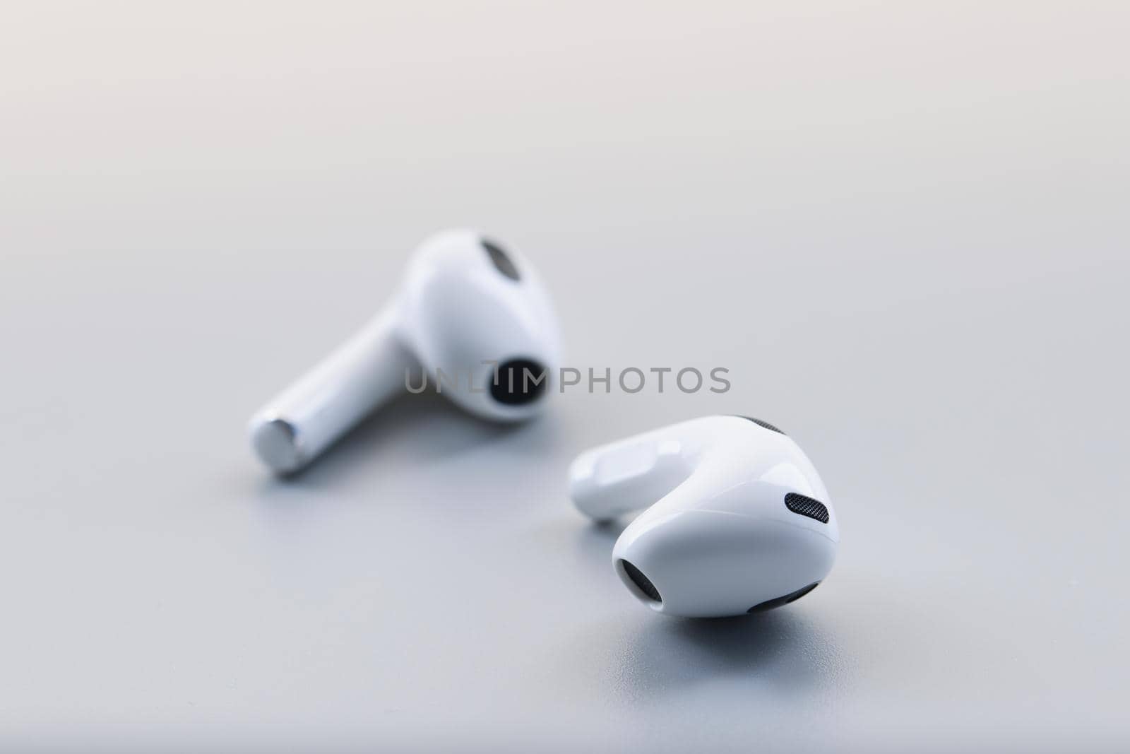 Close-up of pair of white wireless headphones on grey background, modern device to listen music or talk. Technology, earphones, trendy, popular concept