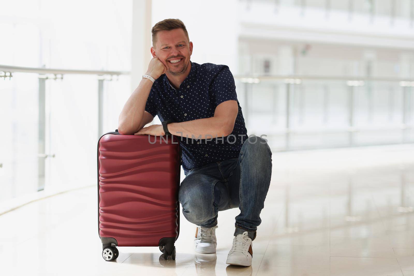 Portrait of happy smiling man posing near suitcase, planning trip abroad, wait for departure in airport. Middle aged man go travelling. Tourism concept