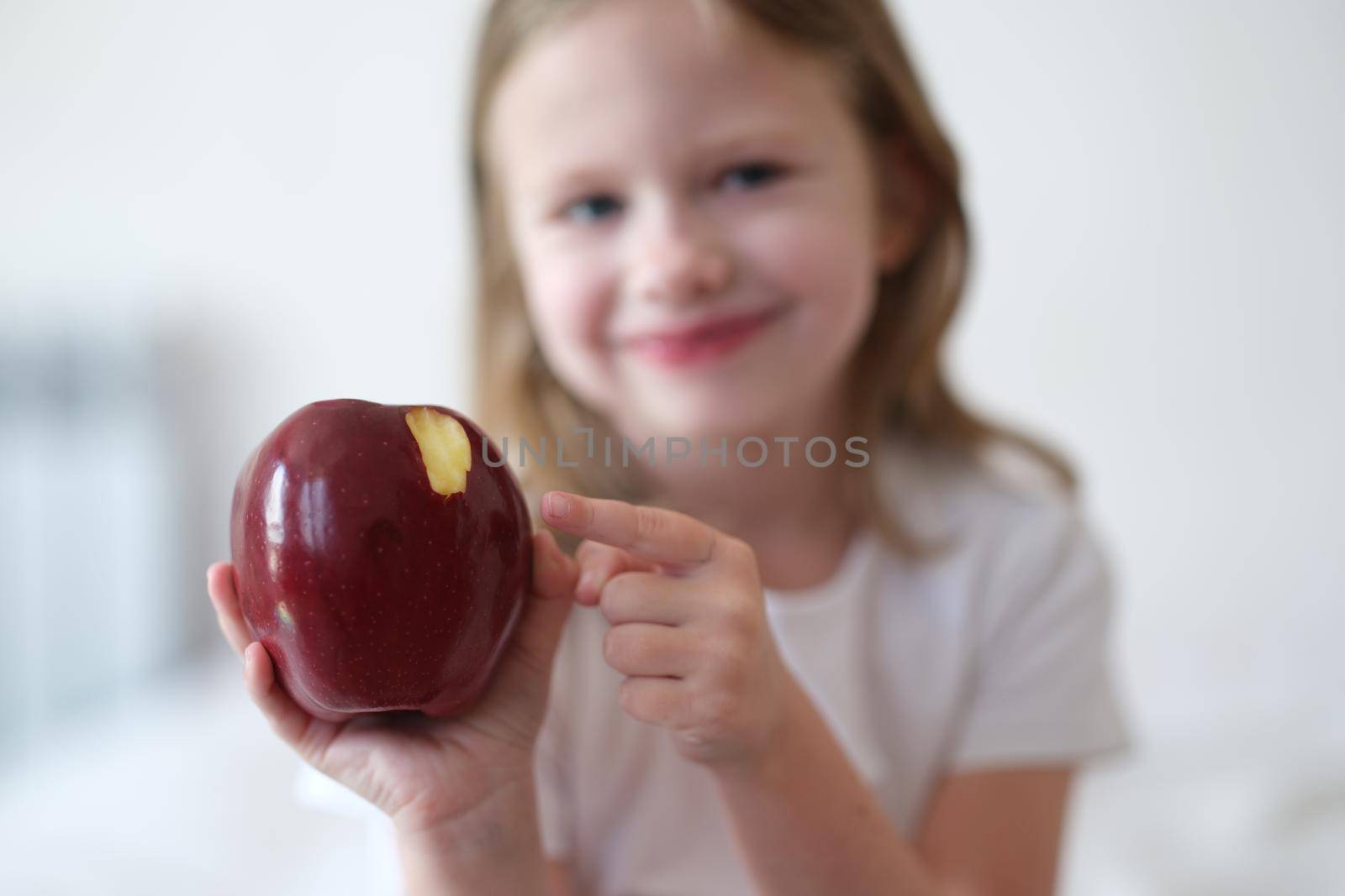 Beautiful little smiling girl eats red ripe apple. Benefits of apples for body concept