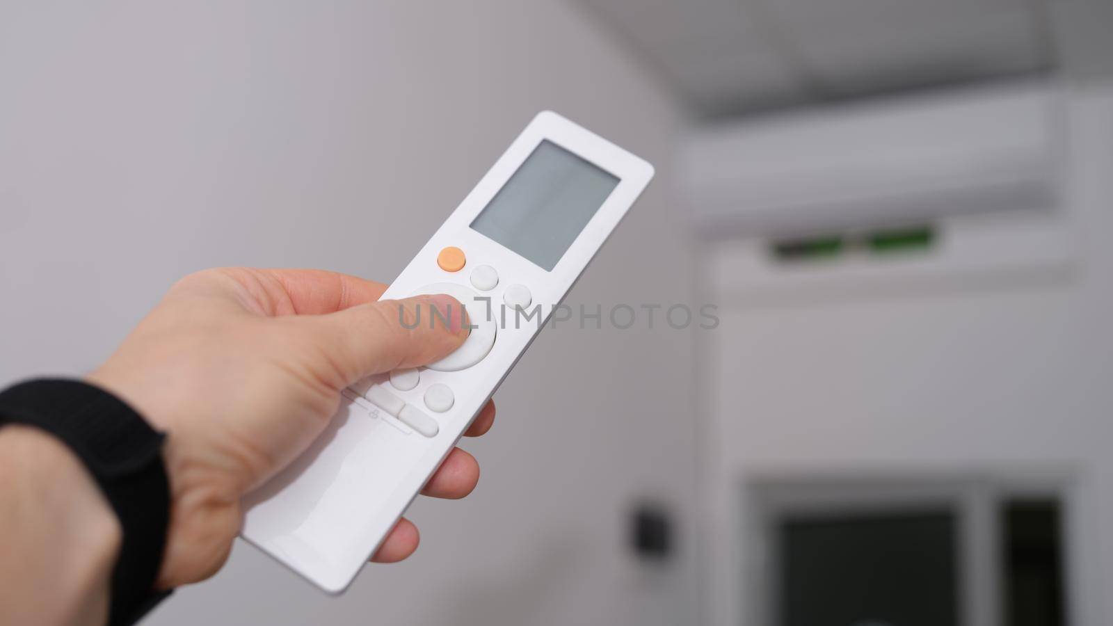 Hand with remote control is directed to air conditioner in room. Climate control indoor concept