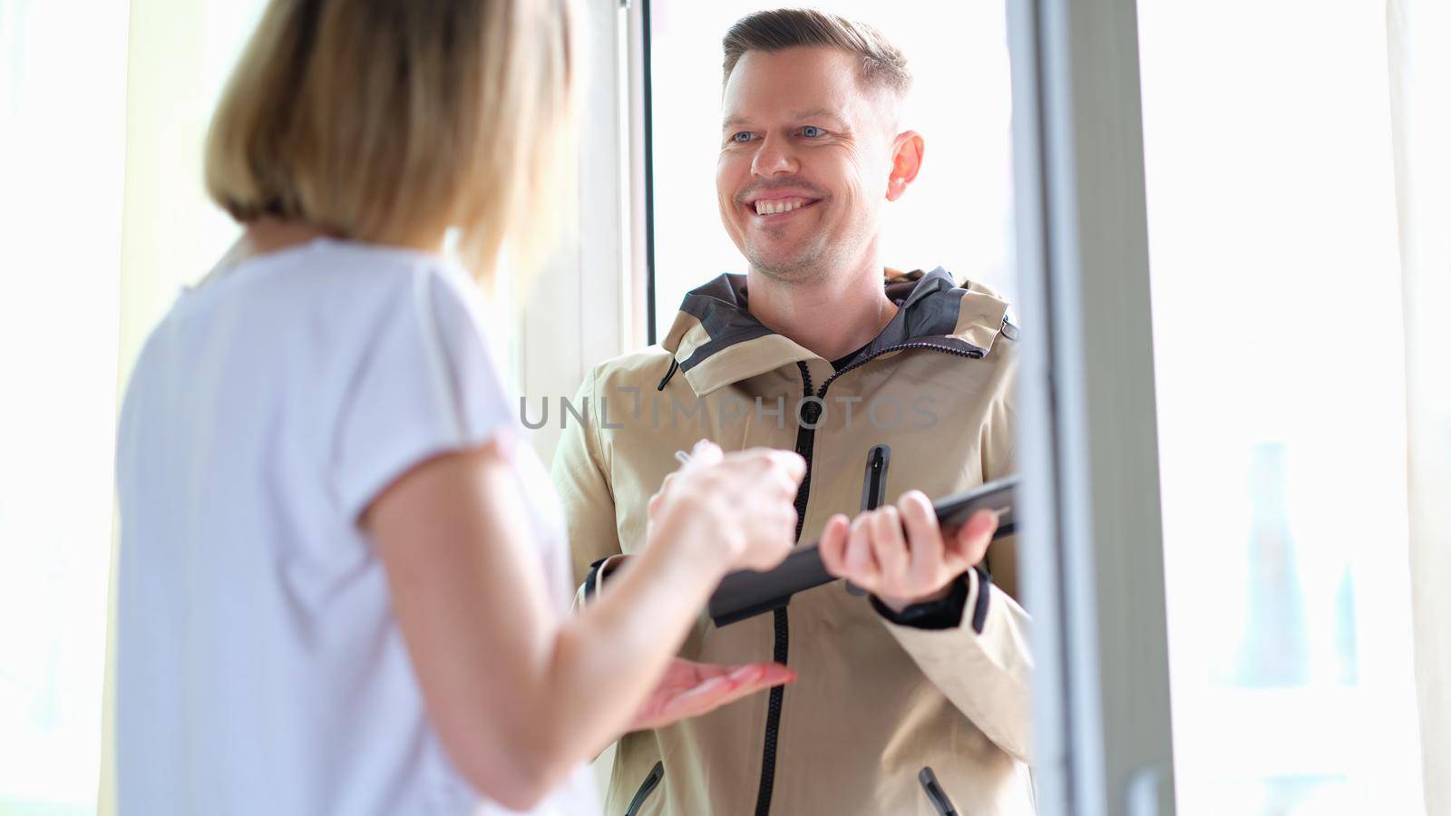 Woman signs on a tablet for parcel from courier at home. Delivery of goods and logistics concept