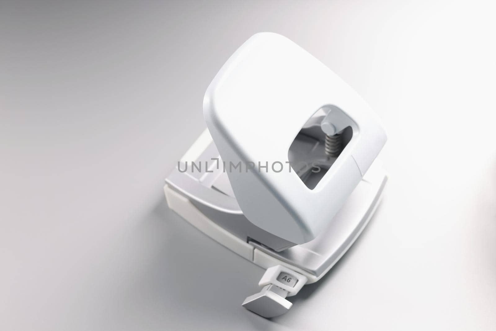 Close-up of white hole punch tool for paper, office accessory on grey background, simple in use, equipment for making holes in papers. Stationery concept