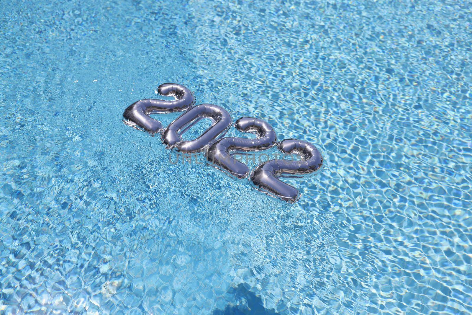 Top view of silver foil numbers floating on blue clean swimming pool water, festive decor for new year party on resort hotel territory. New year concept