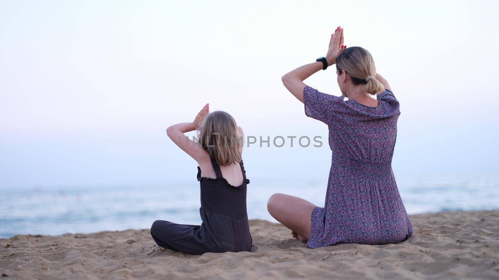 Mother and daughter do yoga meditate in lotus position on beach. by kuprevich