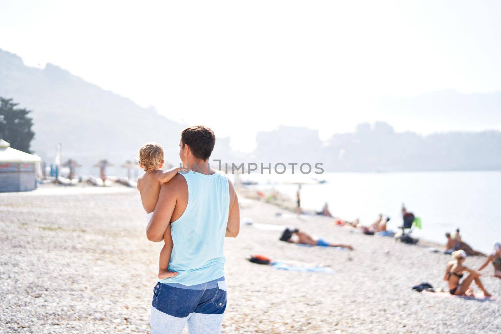 Dad with a little daughter in his arms walks on a pebble beach. High quality photo