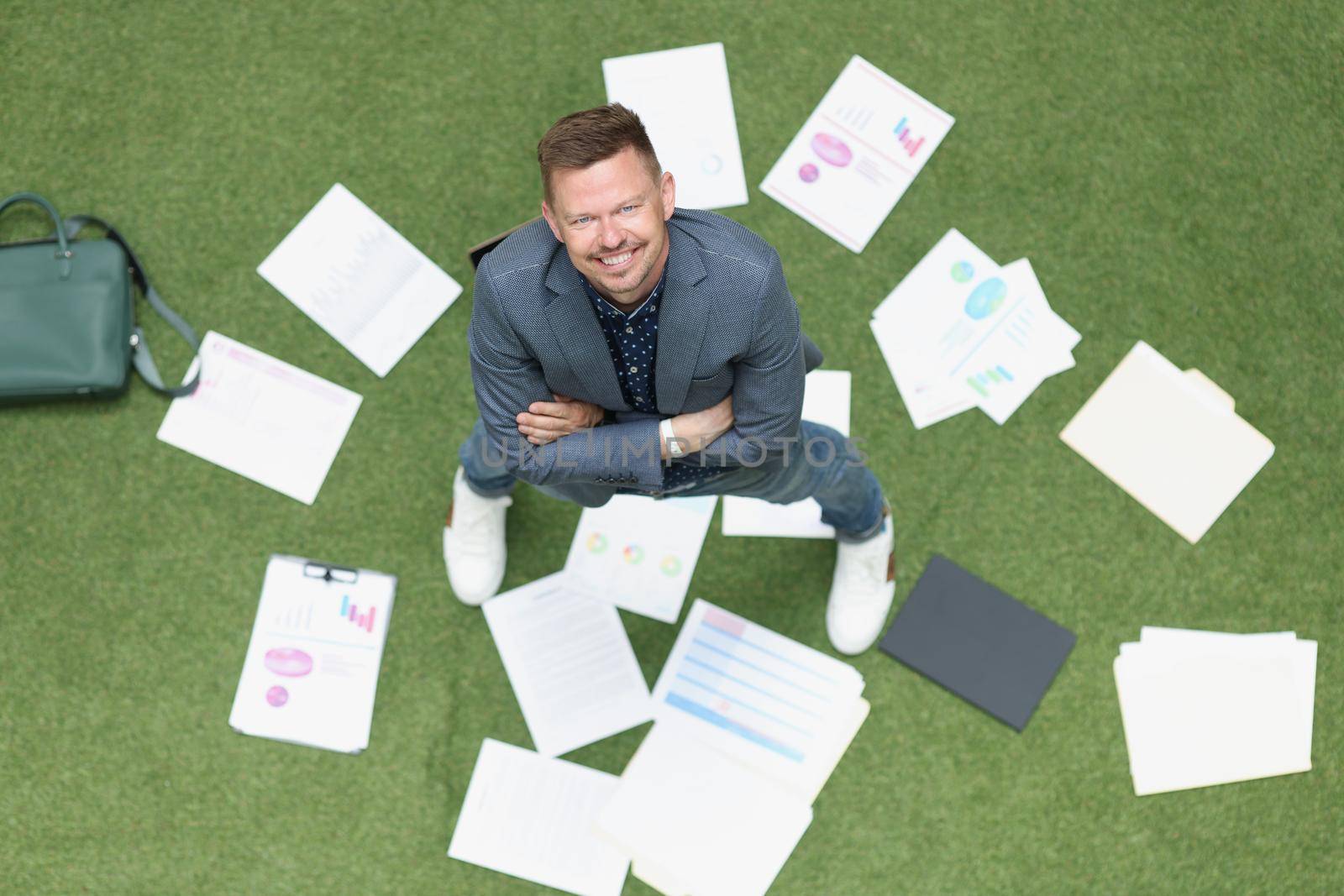 Happy businessman scattered documents on green lawn, top view. Concept vacation, freedom from work, successful project