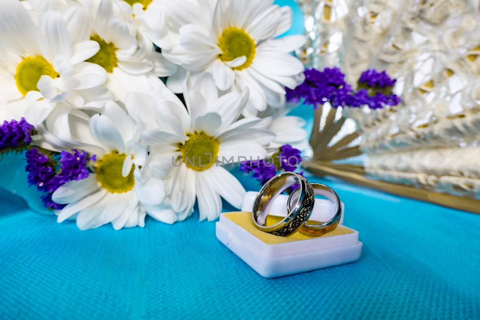 Wedding bouquet of bride. wedding card with original rings in a white box, a bouquet of white chrysanthemums or daisies and a white lace fan on a blue background
