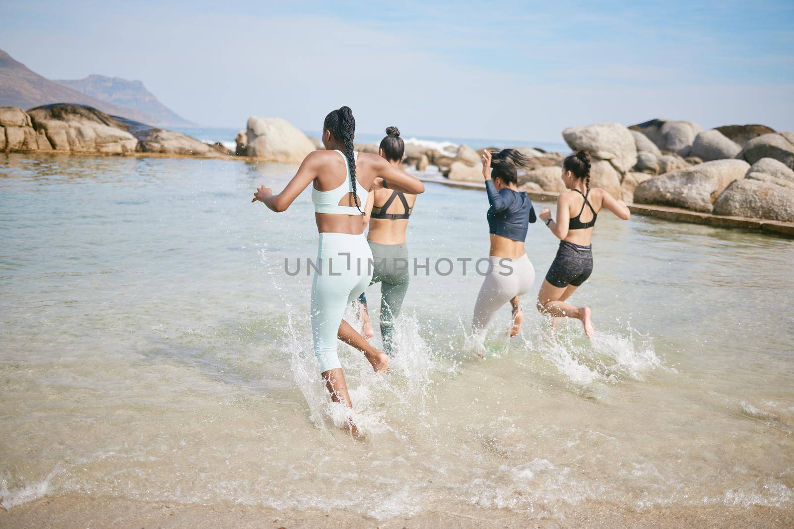 Never forget your inner child. a group of friends splashing around at the beach after a workout. by YuriArcurs