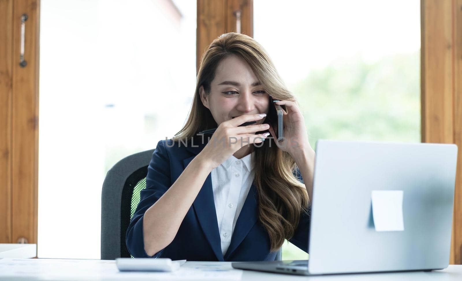 Beautiful young Asian businesswoman charming smiling and talking on the mobile phone in the office. by wichayada