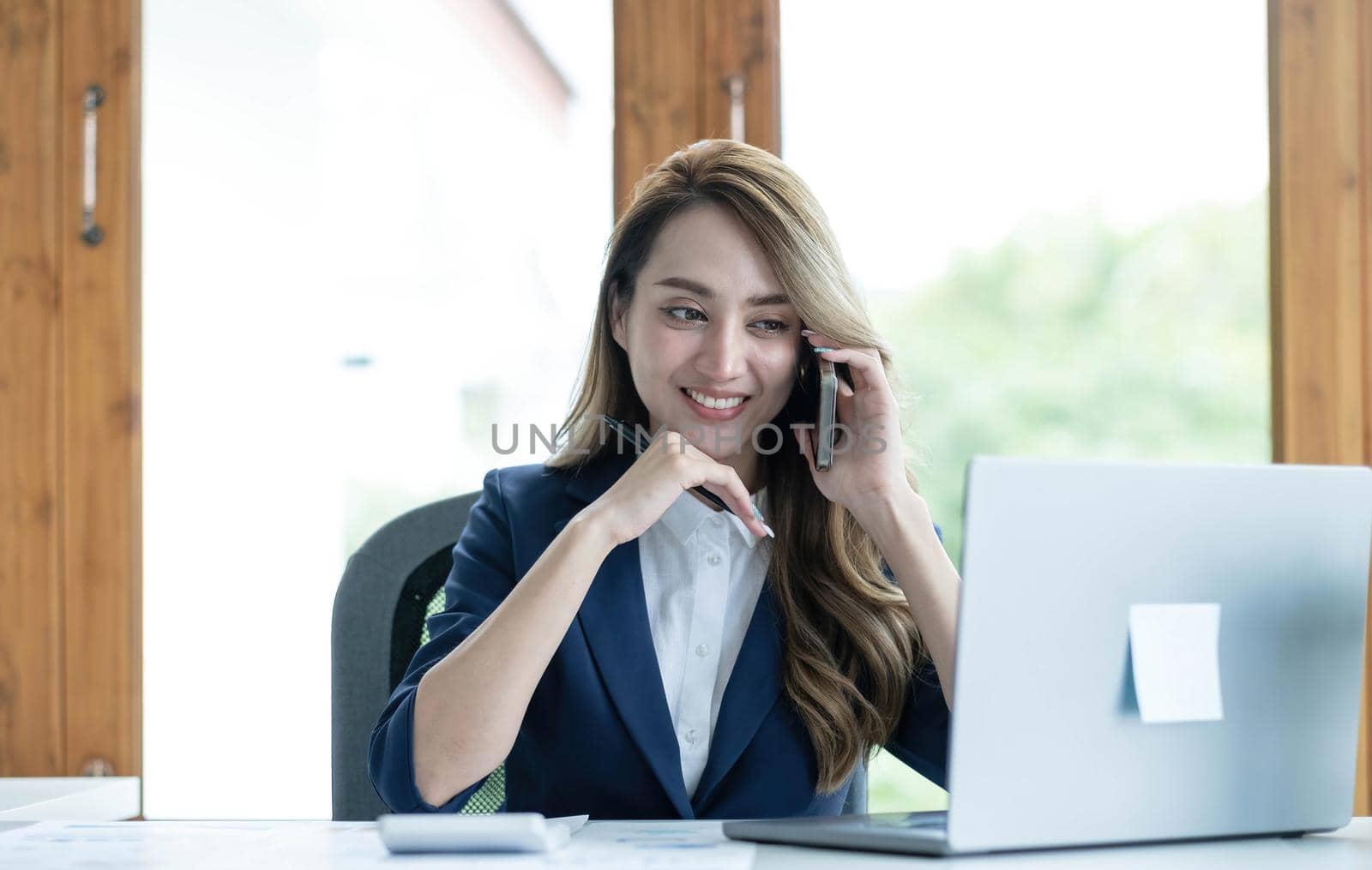 Beautiful young Asian businesswoman charming smiling and talking on the mobile phone in the office. by wichayada