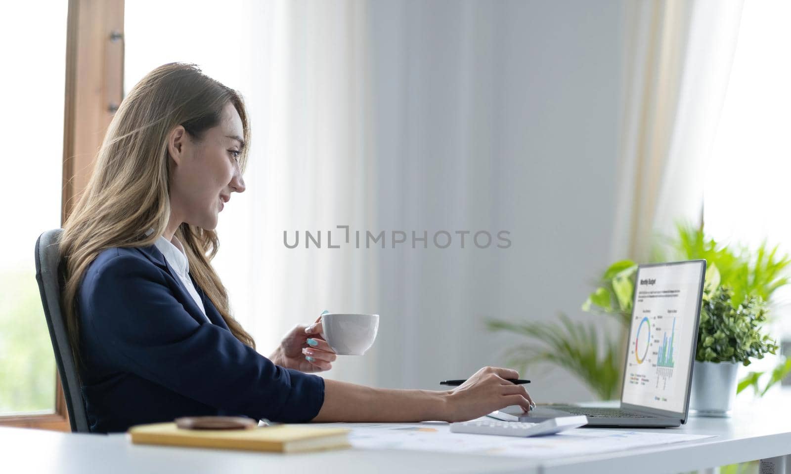 Beautiful young Asian businesswoman smiling holding a coffee mug and laptop working at the office..