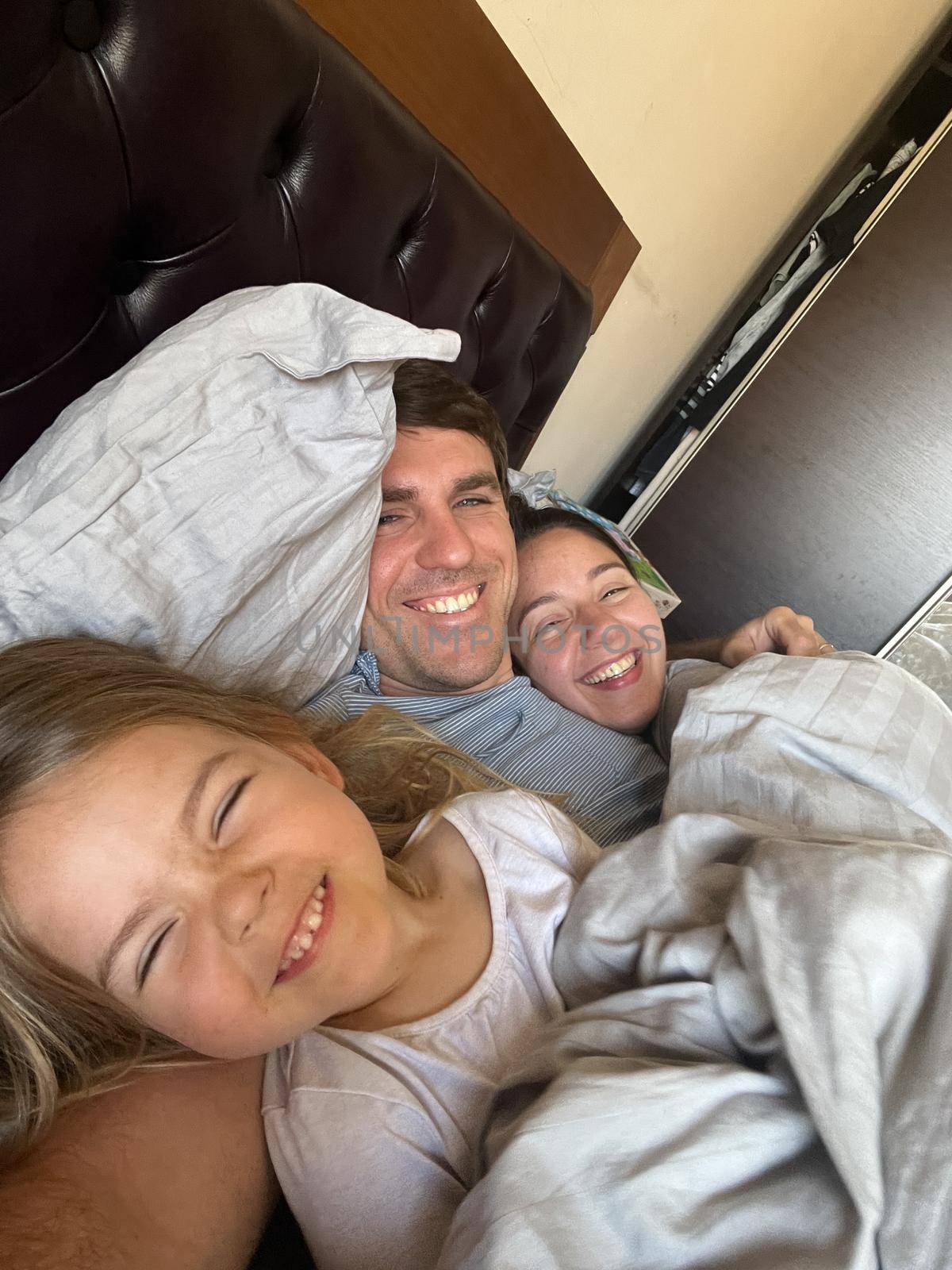 Smiling mom, dad and little girl lying in bed. High quality photo