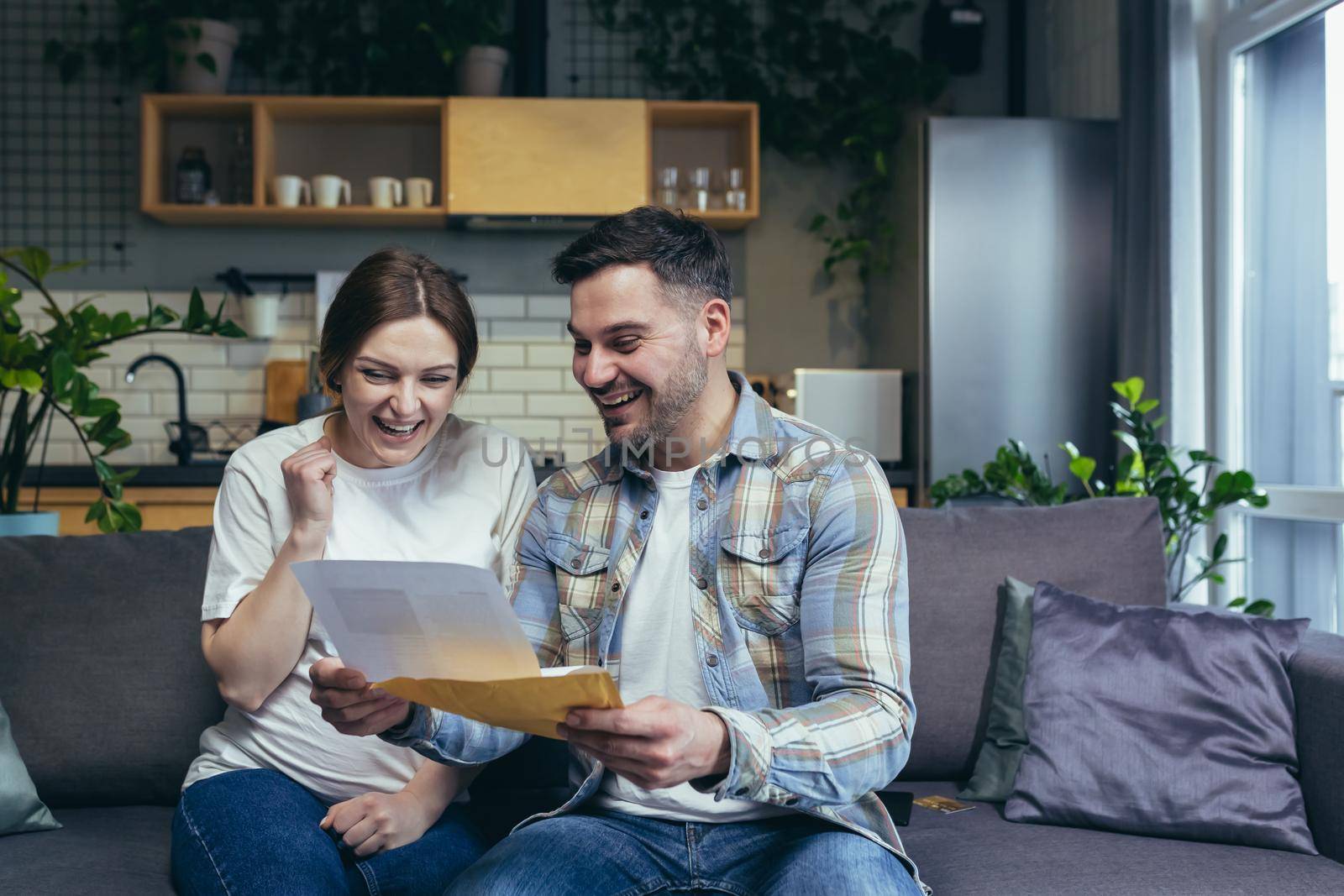 Young family. The man and the pregnant woman received a letter, documents, a mortgage permit, and a loan. Very happy. Sitting on the couch at home.