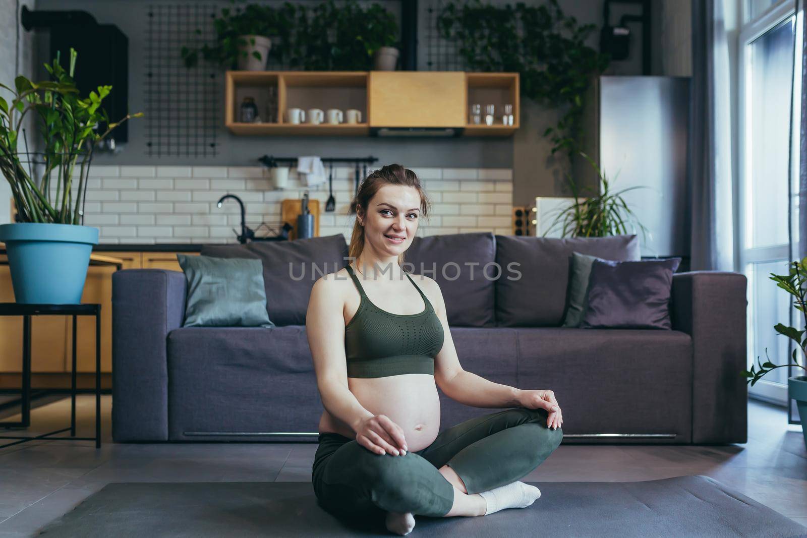 A pregnant woman meditates and practices yoga in a lotus position at home