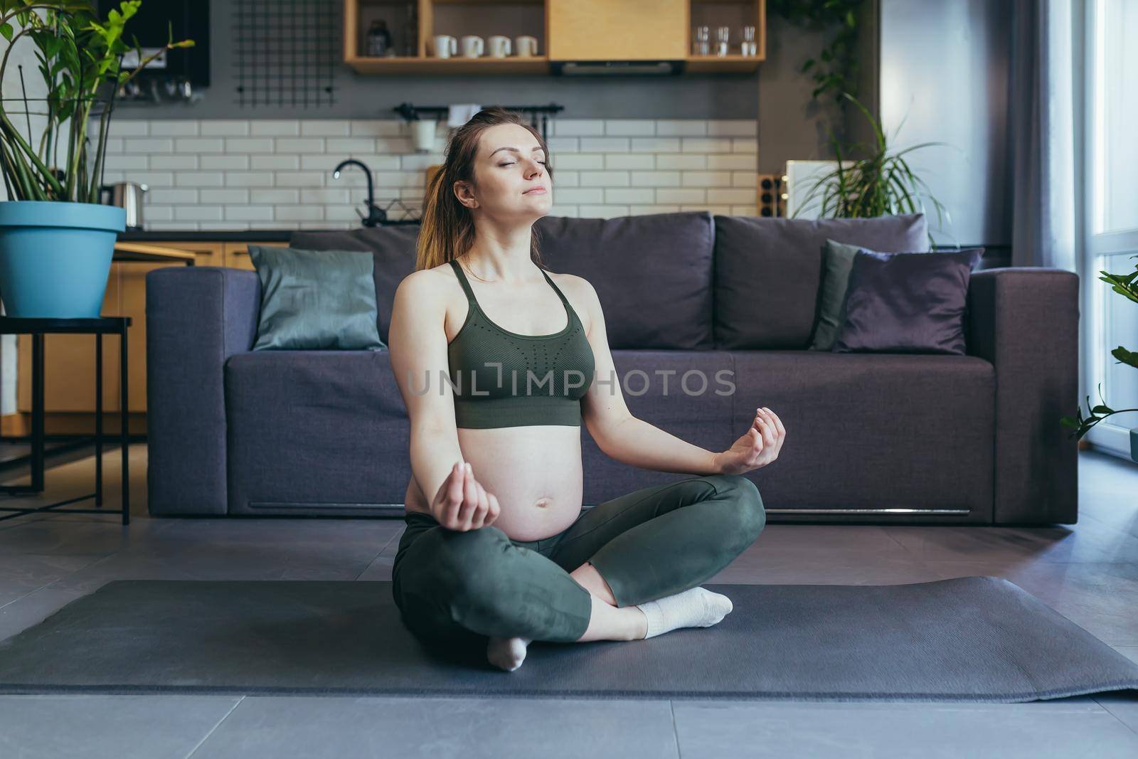 A pregnant woman meditates and practices yoga in a lotus position at home by voronaman