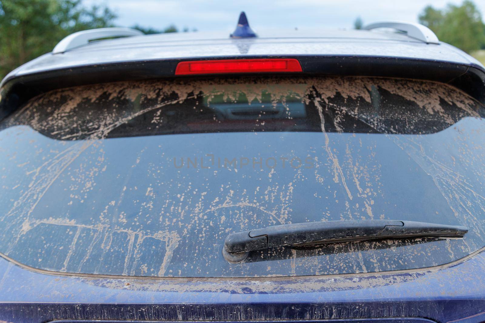 Dirty car glass with wiper and third brake light, rear window covered with a layer of dust and sand.